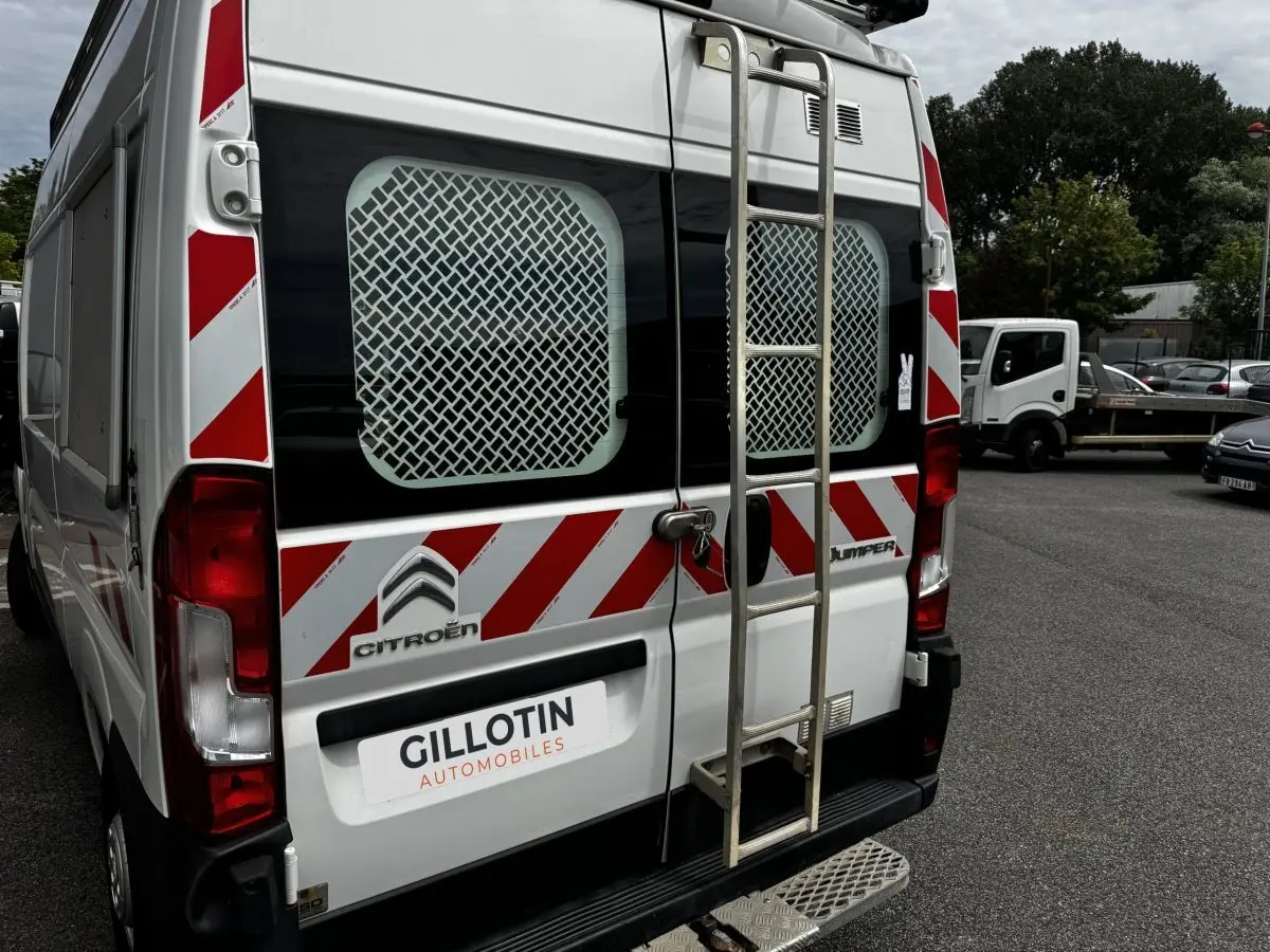 Vue arrière d’un Citroën Jumper blanc avec échelle métallique et bandes rouges et blanches de signalisation.