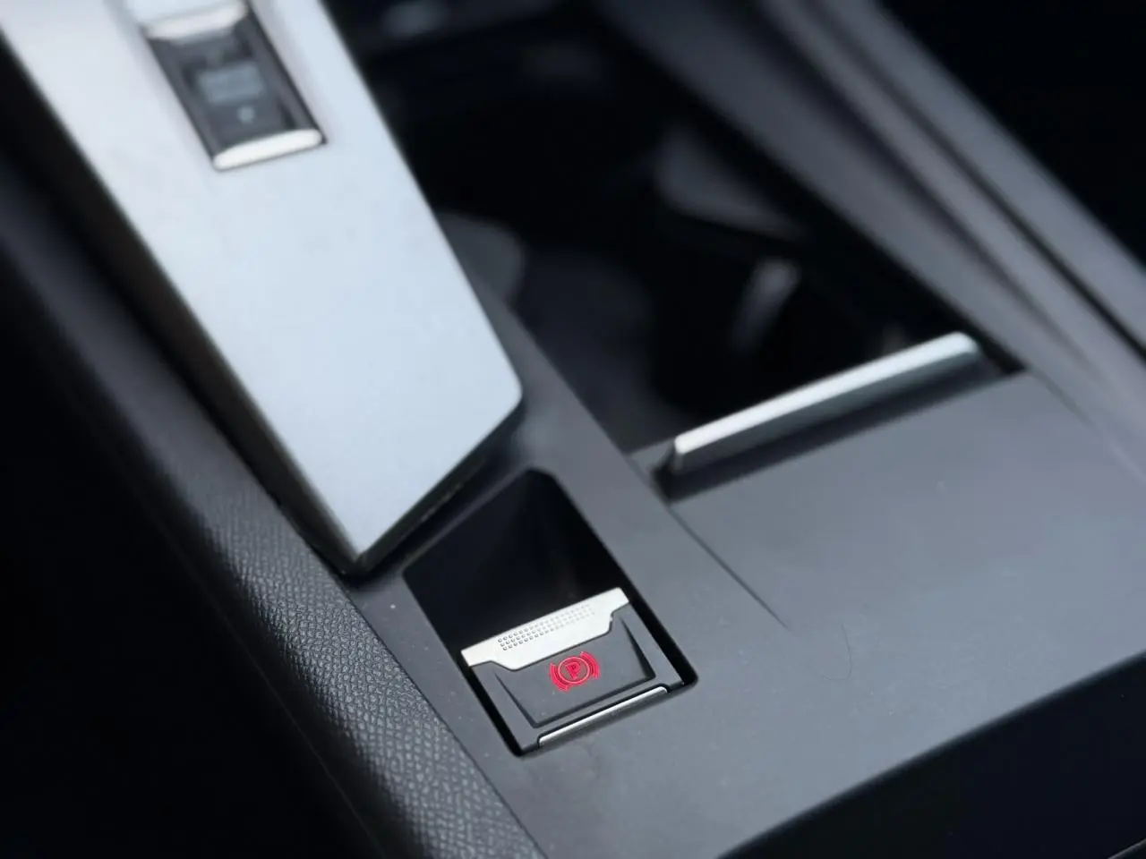 Gros plan sur le frein de parking électrique rouge dans la console centrale noire du Peugeot 308 Hybrid 2025.