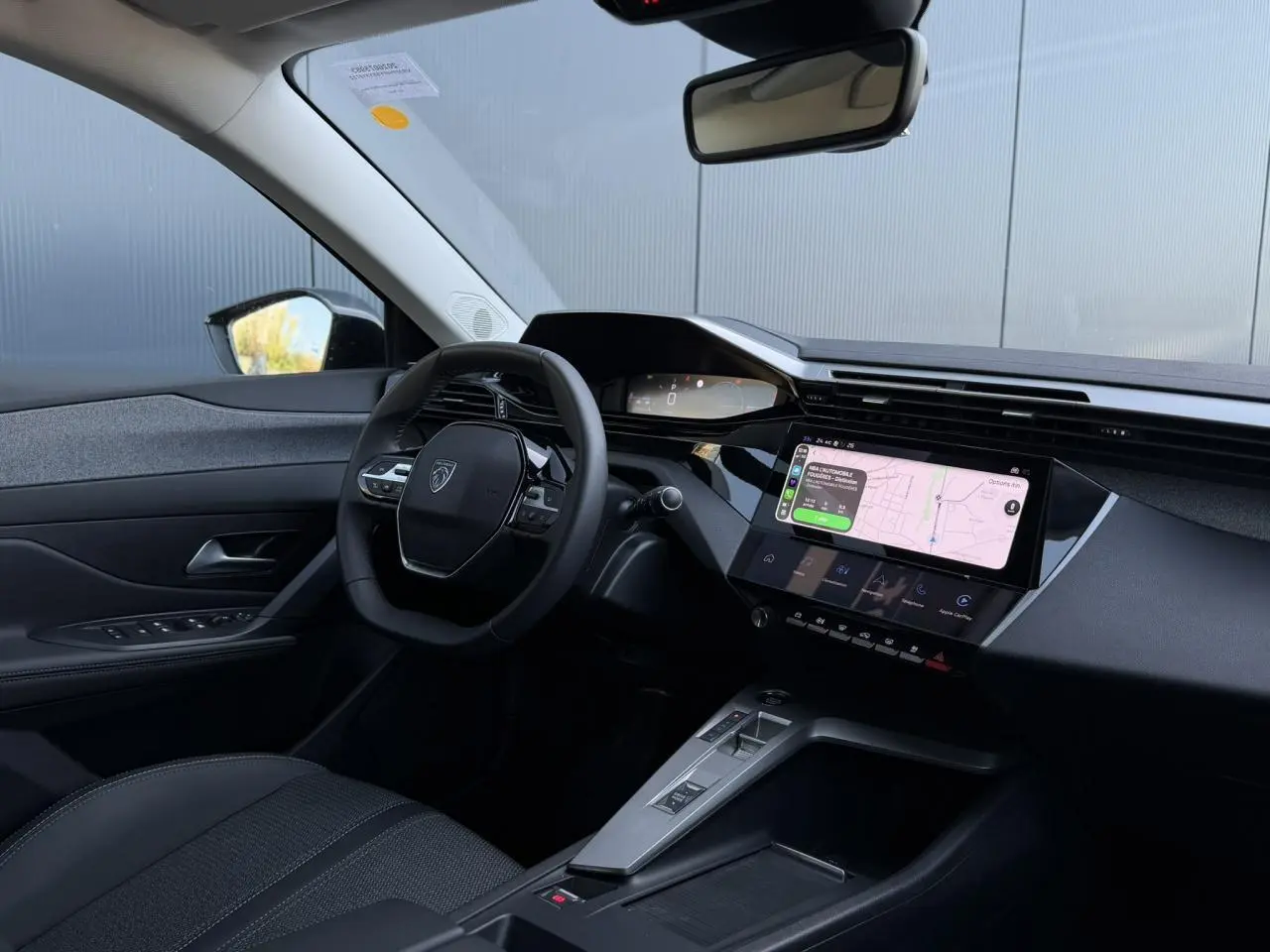 Intérieur Peugeot 308 Hybrid 2025 vu côté conducteur, tableau de bord noir avec écran tactile 10 pouces et volant compact.