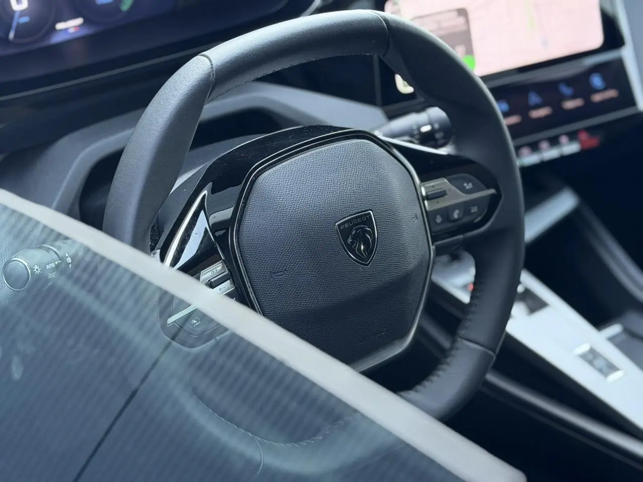 Gros plan sur le volant cuir noir de la Peugeot 308 Hybrid 145, avec tableau de bord numérique et écran tactile visible.