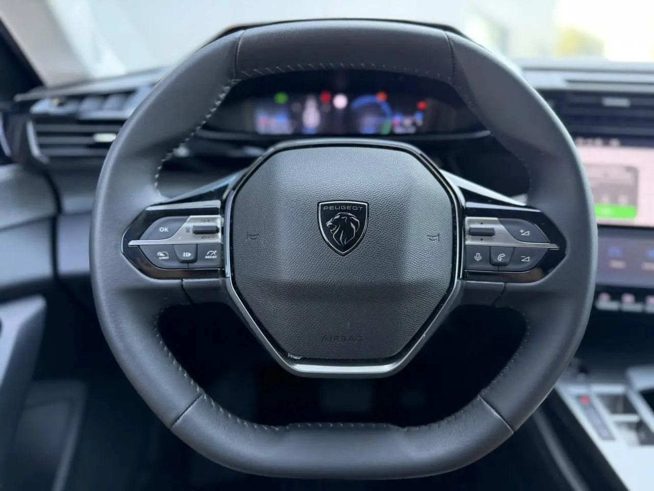 Volant cuir noir au design hexagonal avec logo Peugeot, vue centrée sur le poste de conduite intérieur moderne.
