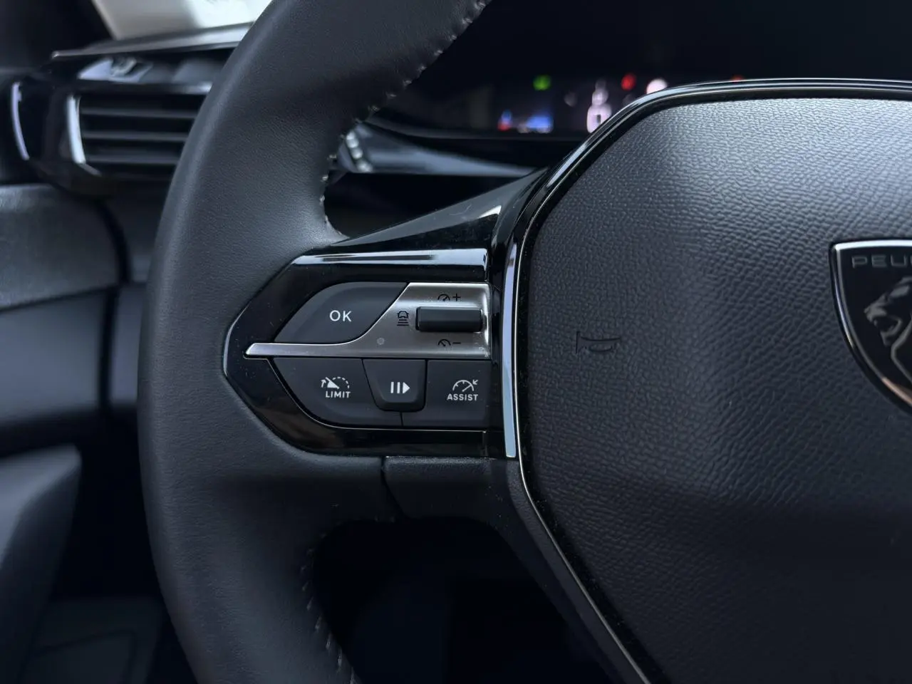 Gros plan sur la partie gauche du volant noir de la Peugeot 308 Hybrid 2025 avec commandes intégrées et logo lion.