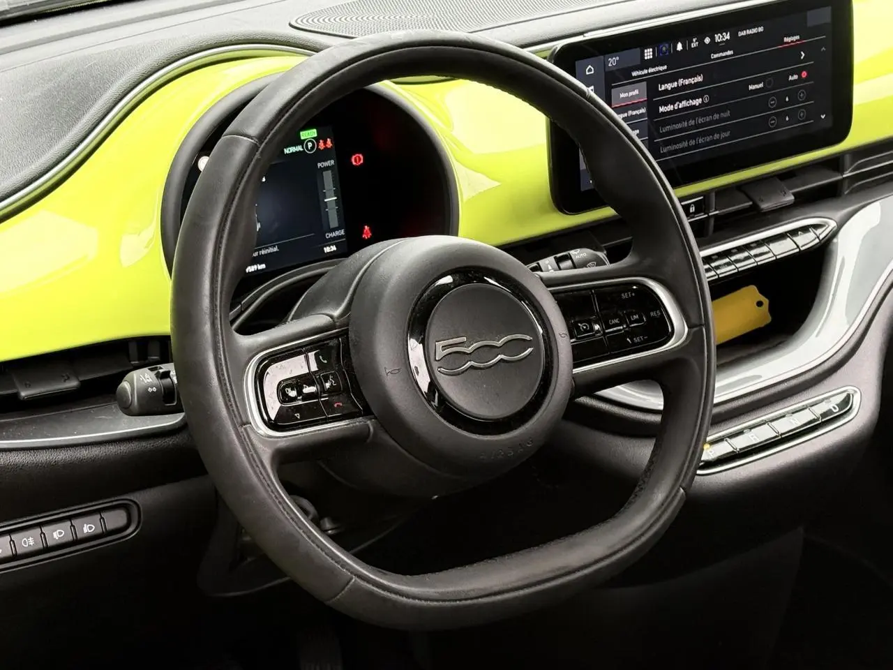 Vue intérieure centrée sur le volant noir et le tableau de bord jaune Acid de la FIAT 500 électrique 2024.