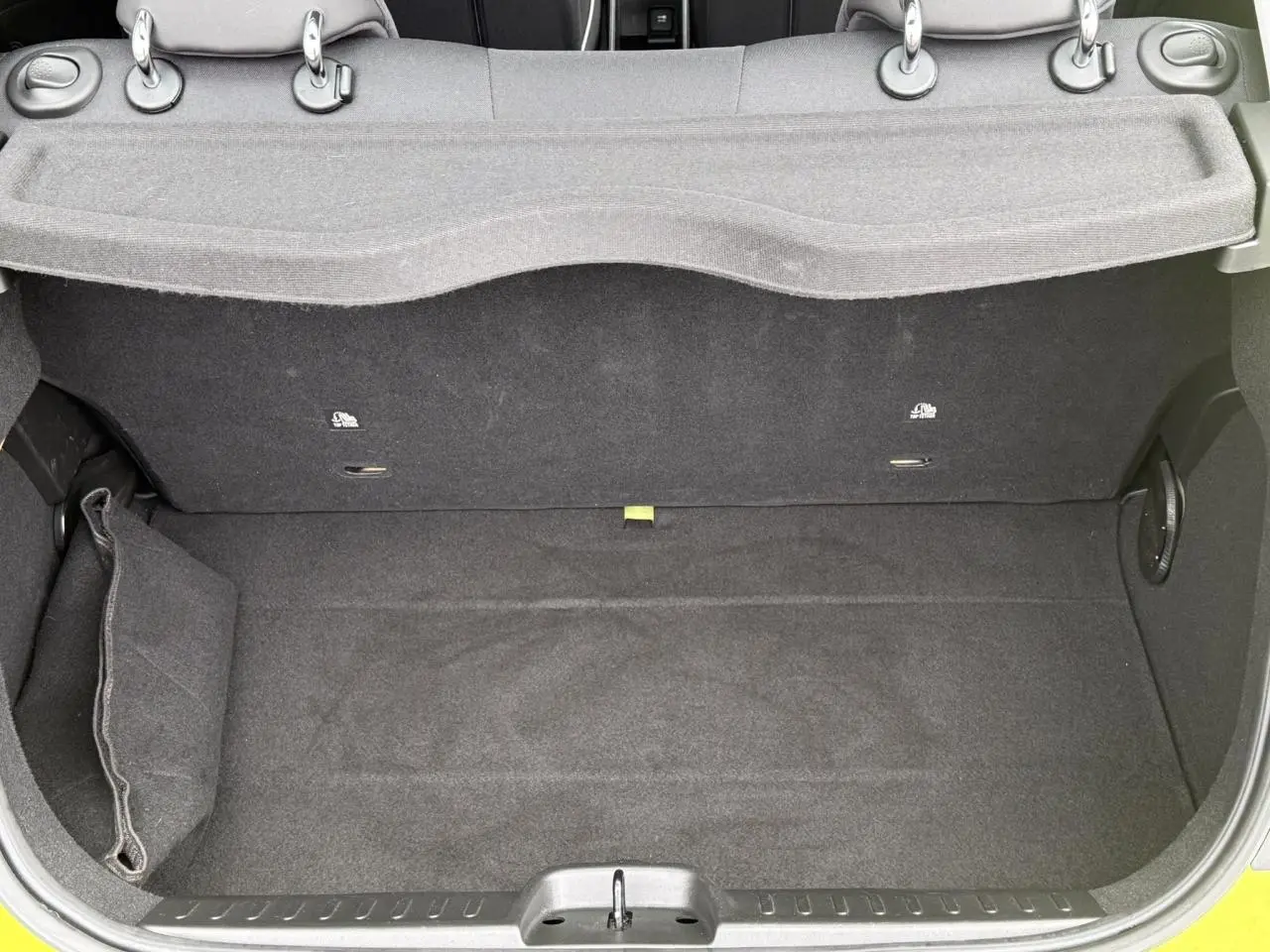 Coffre ouvert d'une FIAT 500 électrique 2024 en Jaune Acid, montrant un espace de rangement propre et tapissé de noir.