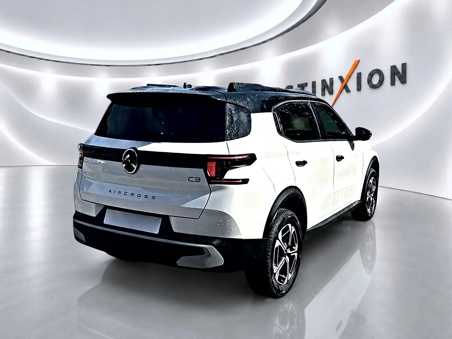Vue 3/4 arrière droite du Citroën C3 Aircross blanc avec toit noir et jantes alu dans un showroom moderne.