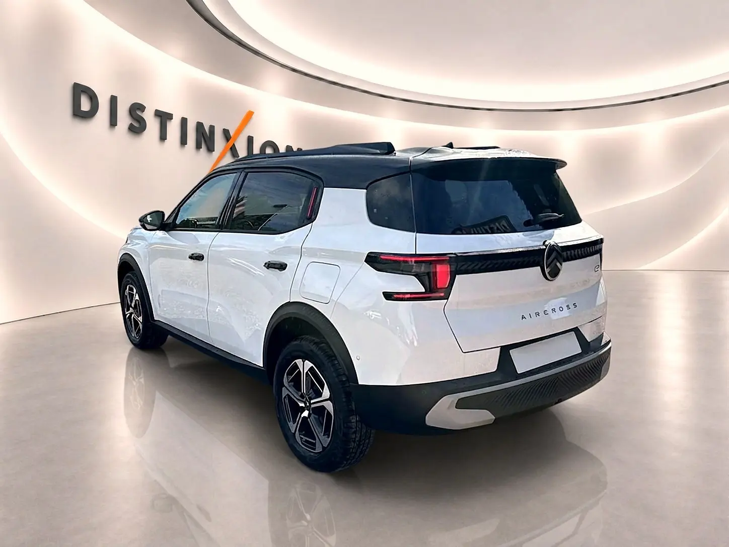 Vue 3/4 arrière droite d'un Citroën C3 Aircross blanc avec toit noir et jantes alu en intérieur showroom.
