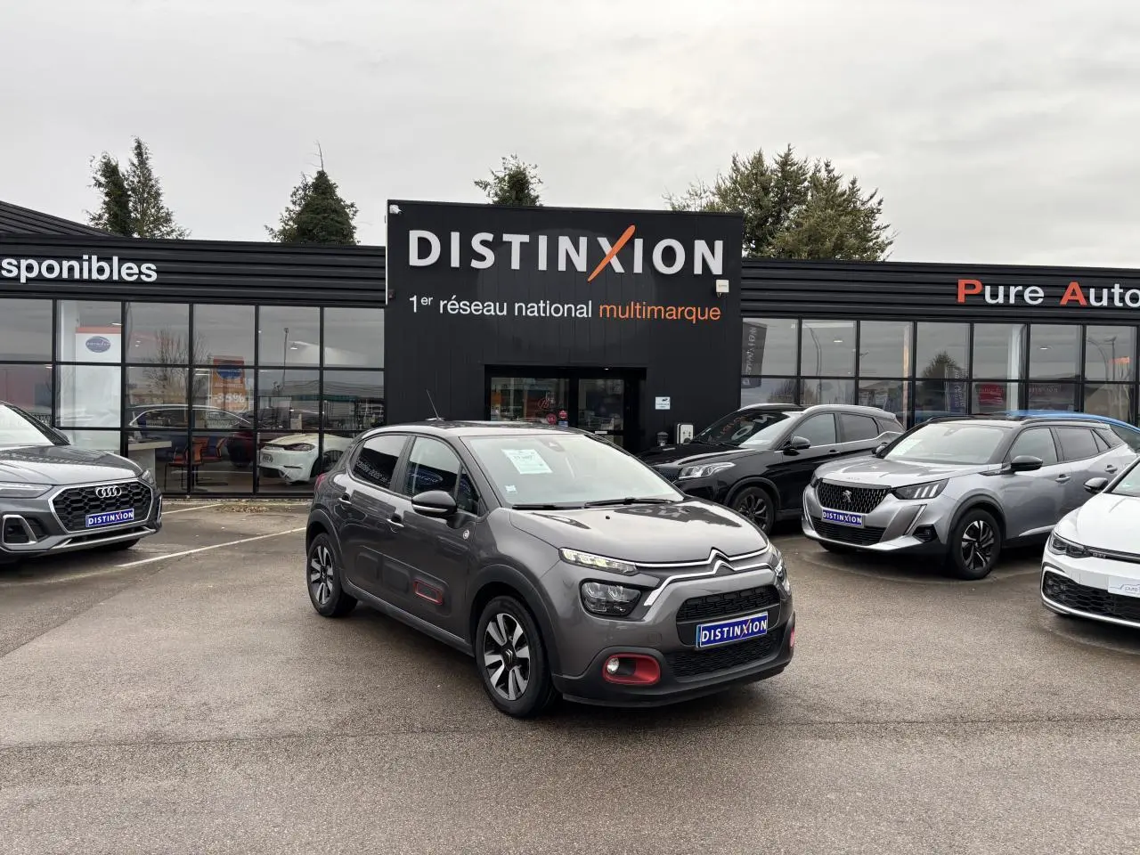 Citroën C3 gris foncé vue 3/4 avant droit avec décorations rouges sur les portes, stationnée devant un concessionnaire Distinxion.