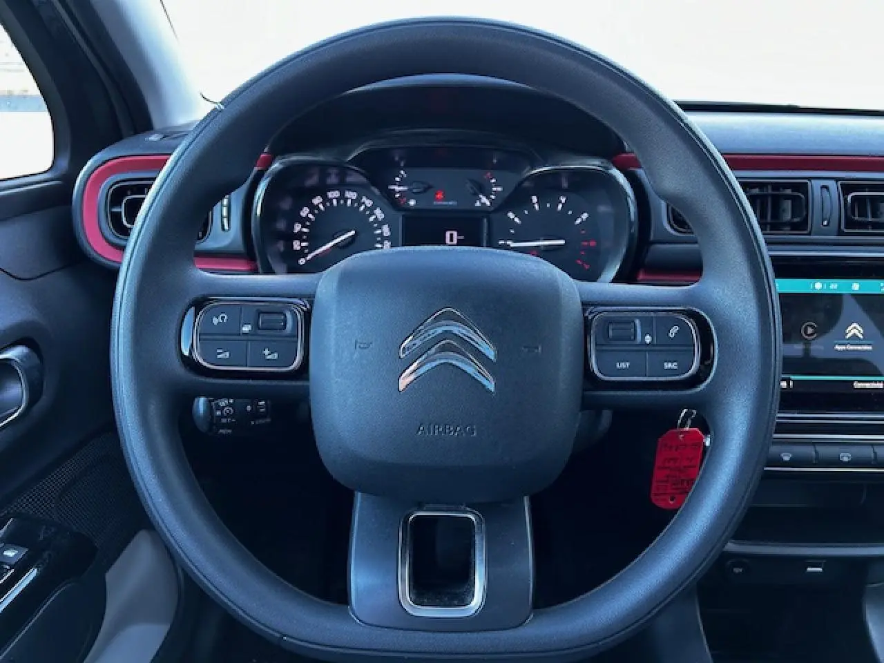 Vue frontale du volant noir de la Citroën C3 III 1.2 PureTech avec tableau de bord et écran tactile rouge et noir.