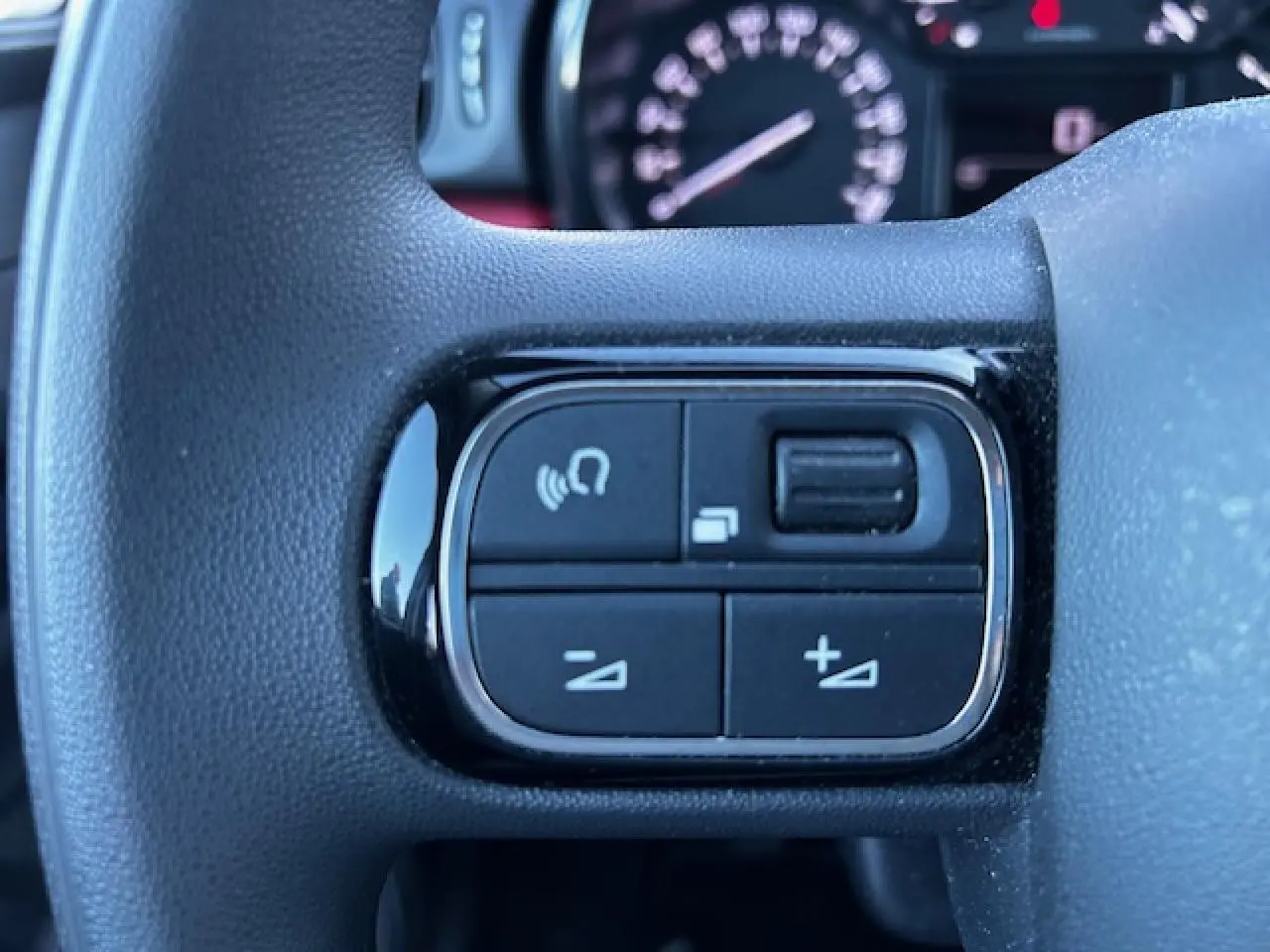 Gros plan sur les commandes audio au volant noir de la Citroën C3 III gris foncé, avec tableau de bord flou en arrière-plan.