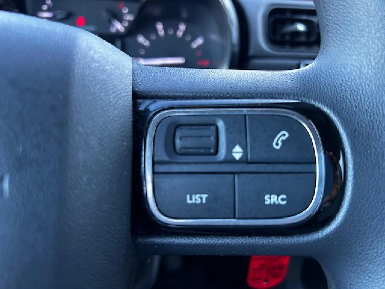 Gros plan sur les commandes audio au volant noir de la Citroën C3 III gris foncé, avec boutons list et appel.