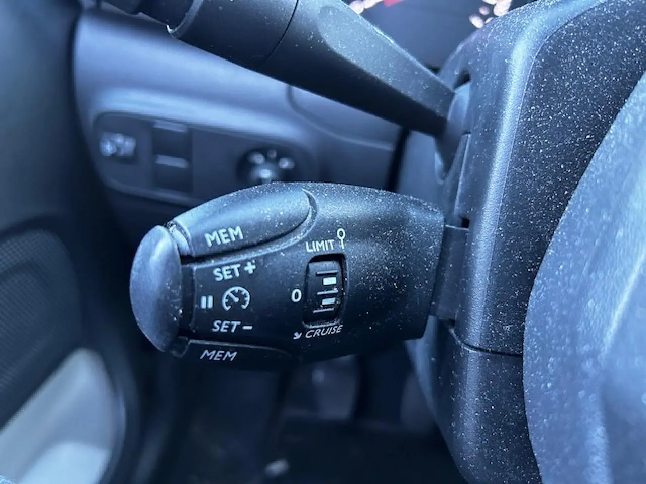 Gros plan sur la commande de régulateur de vitesse noire à gauche du volant dans une Citroën C3 gris foncé.