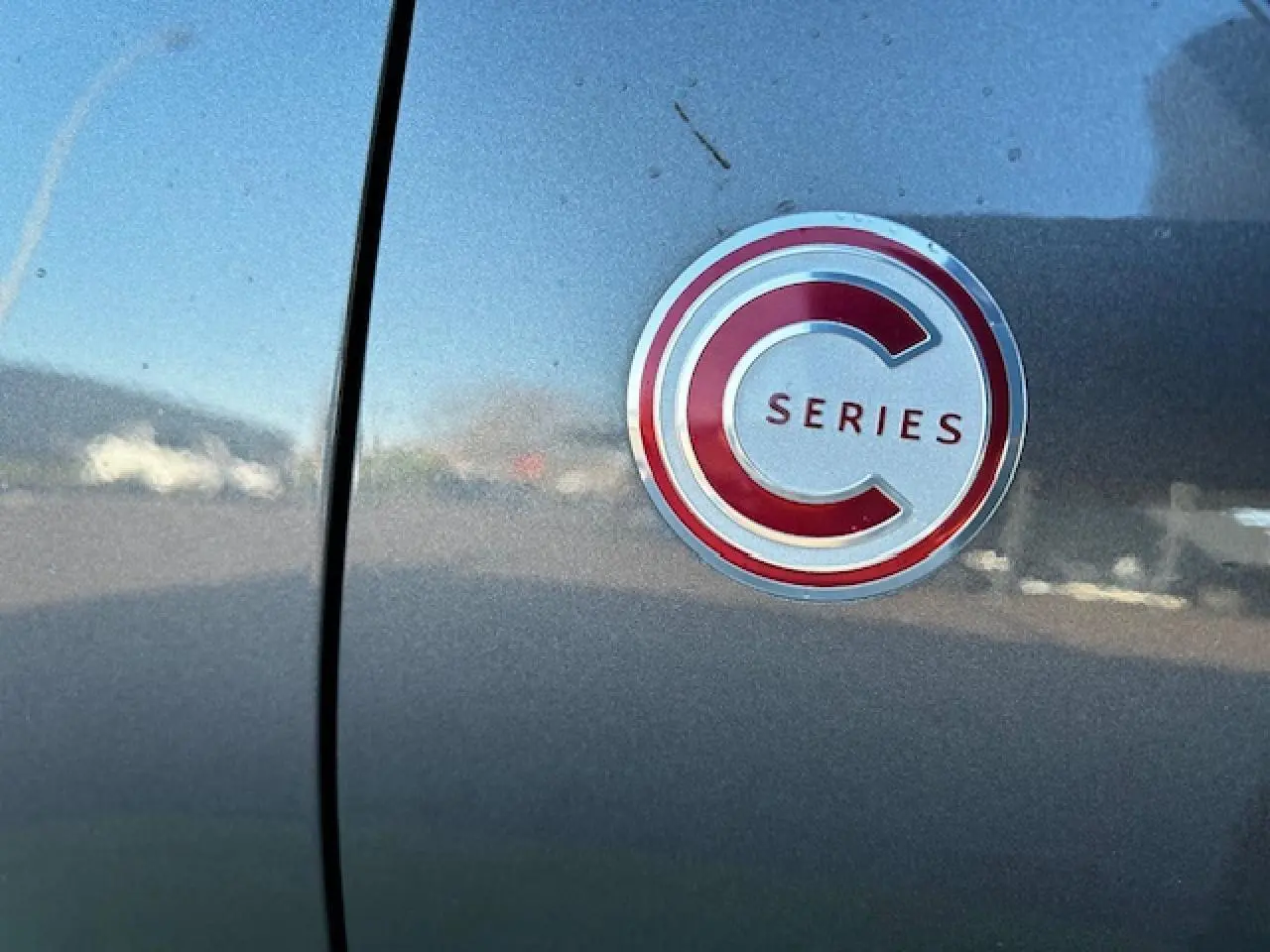 Gros plan sur le badge C-Series rouge et argent sur la porte d'une Citroën C3 gris foncé.
