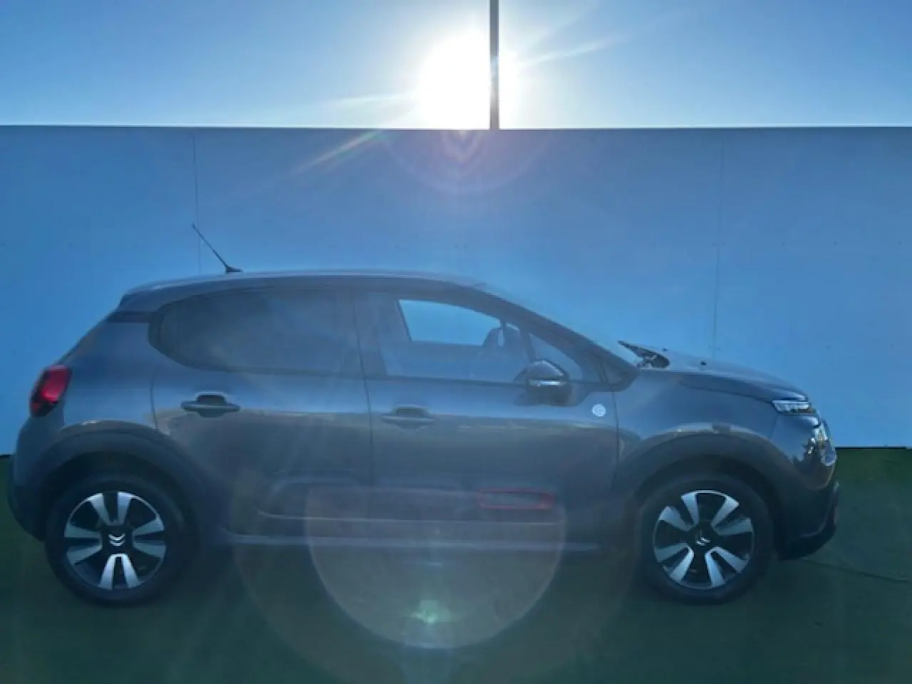 Profil côté gauche d'une Citroën C3 gris foncé 2021 avec enjoliveurs noirs et détails rouges sur les portes