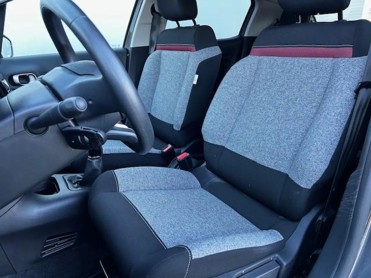 Intérieur avant de la Citroën C3 gris foncé, vue côté conducteur sur les sièges tissu gris et noir avec bande rouge.