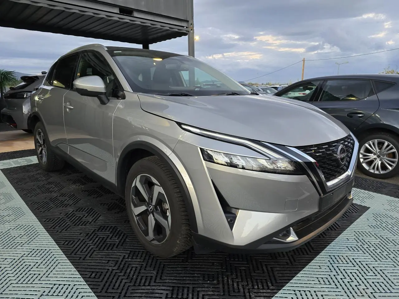 Nissan Qashqai III gris silver en 3/4 avant droit, avec calandre noire et jantes alliage 18 pouces visibles.