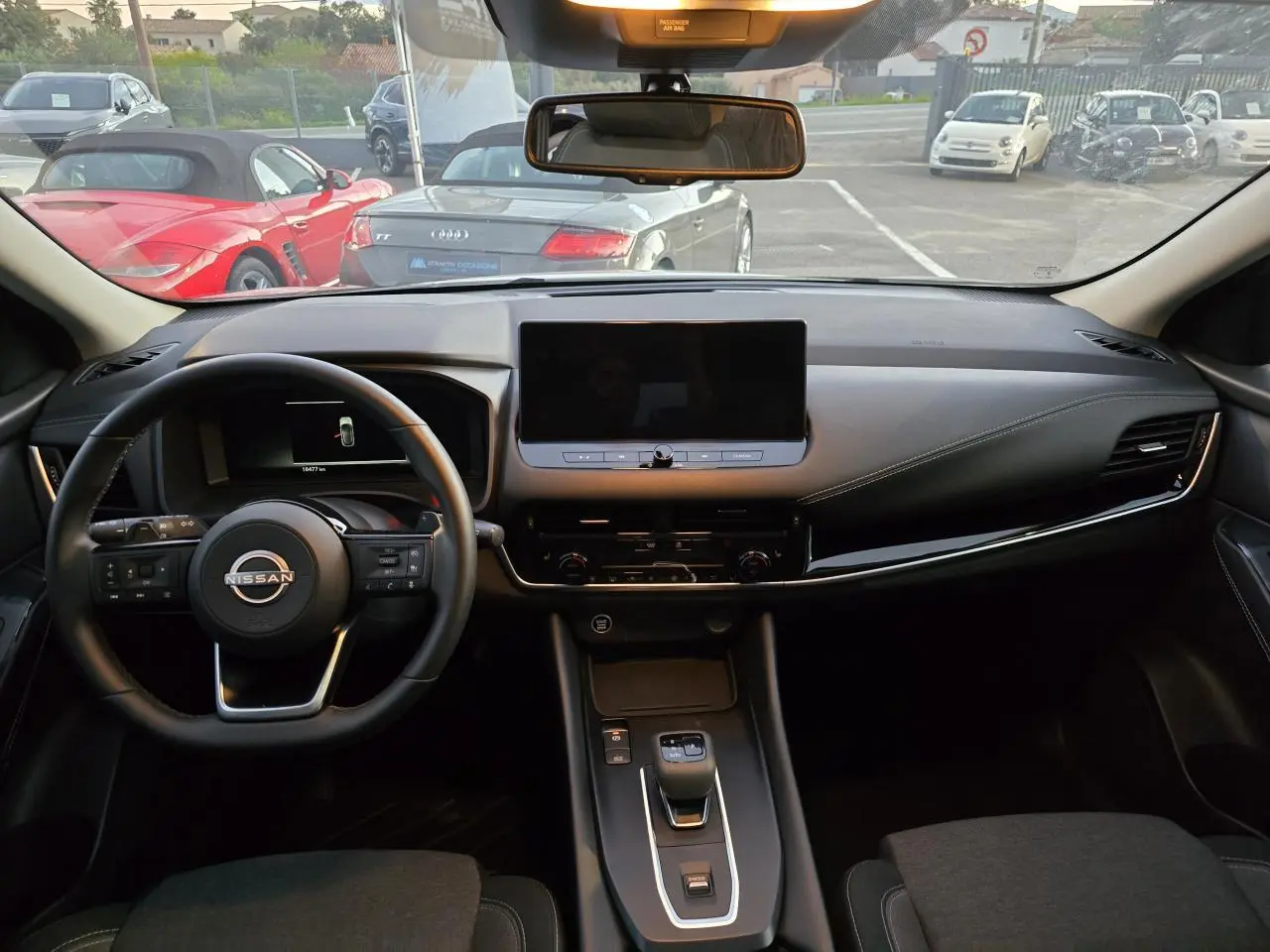 Vue intérieure avant du Nissan Qashqai gris silver 2024, tableau de bord moderne avec écran tactile central et volant cuir.