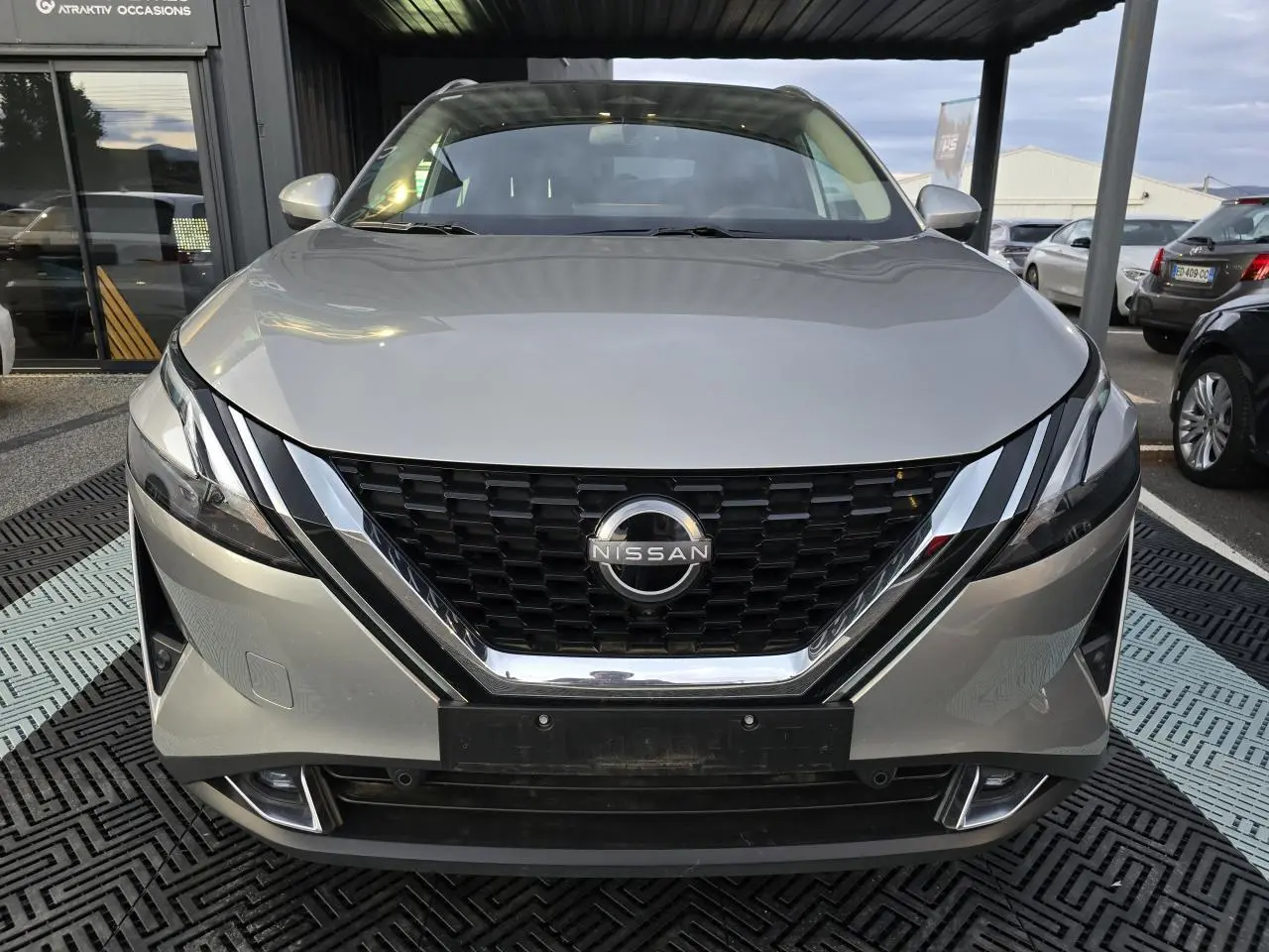 Vue frontale d'un Nissan Qashqai gris silver 2024 avec calandre noire et détails chromés sous un abri.