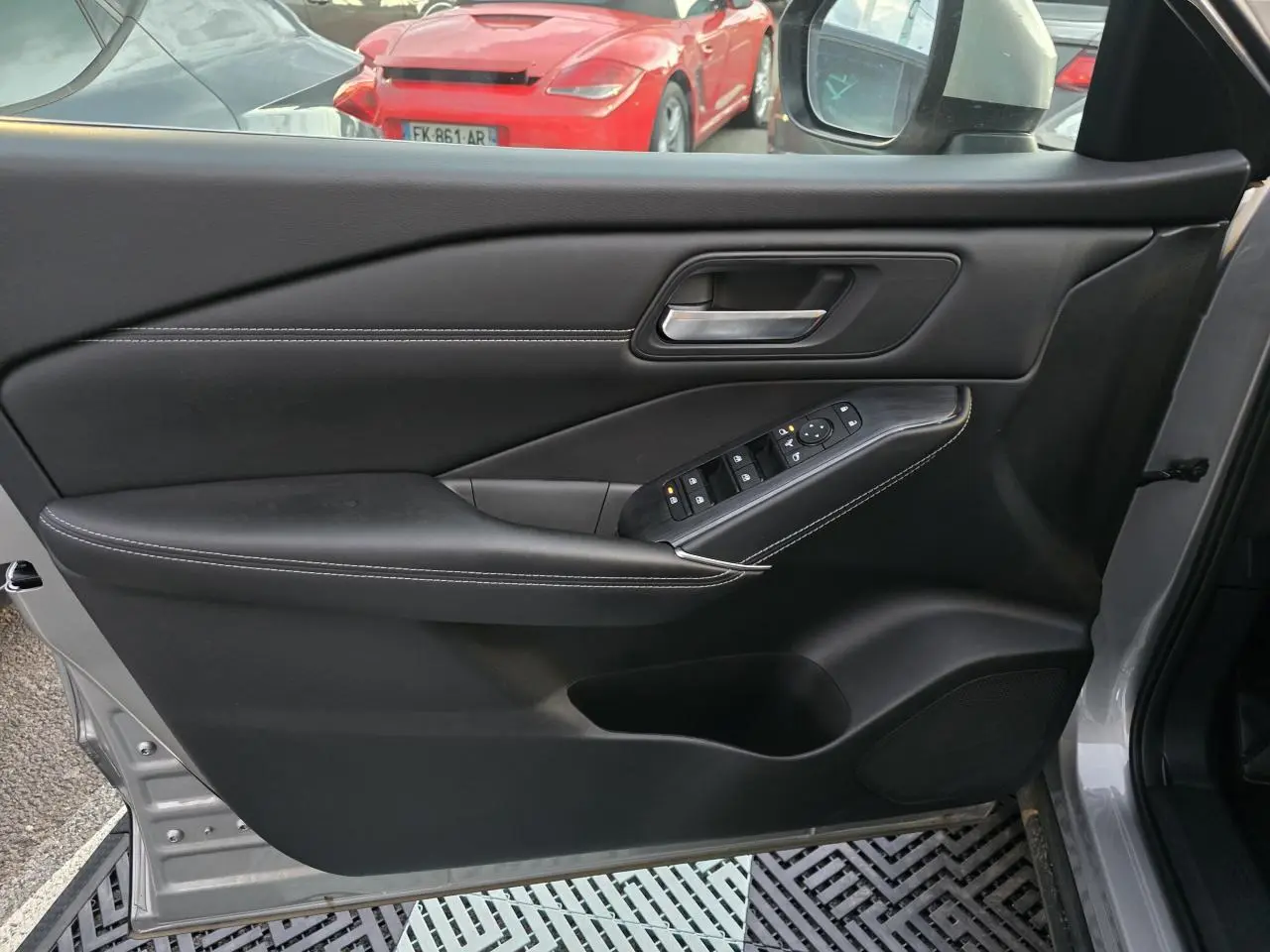 Vue intérieure côté gauche de la porte avant gris silver du Nissan Qashqai 2024 avec commandes de vitres et poignée intégrée.