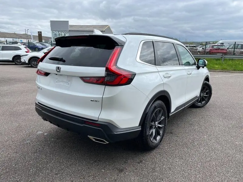 Vue 3/4 arrière droite d'un Honda CR-V blanc platine nacré 2024 avec jantes noires et feux arrière LED en forme de L.