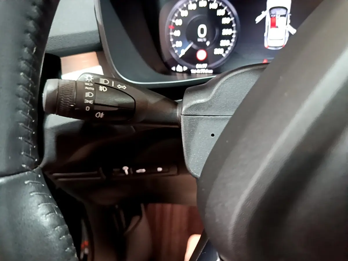 Gros plan sur la manette de commandes d'éclairage à gauche du volant cuir du Volvo XC40 noir, tableau de bord numérique visible.