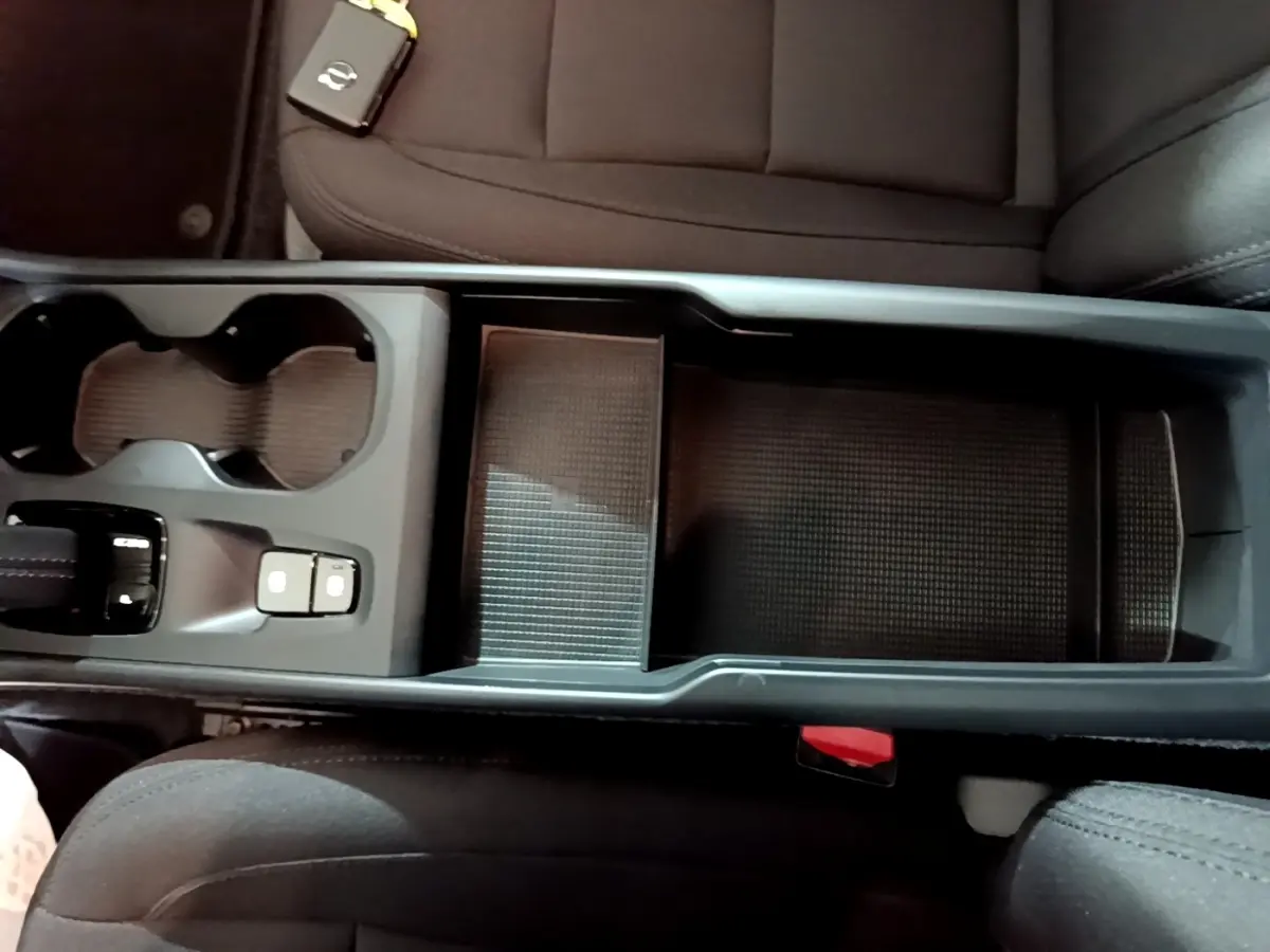 Vue plongeante sur la console centrale noire du Volvo XC40 Recharge T4 avec porte-gobelets et accoudoir ouvert.