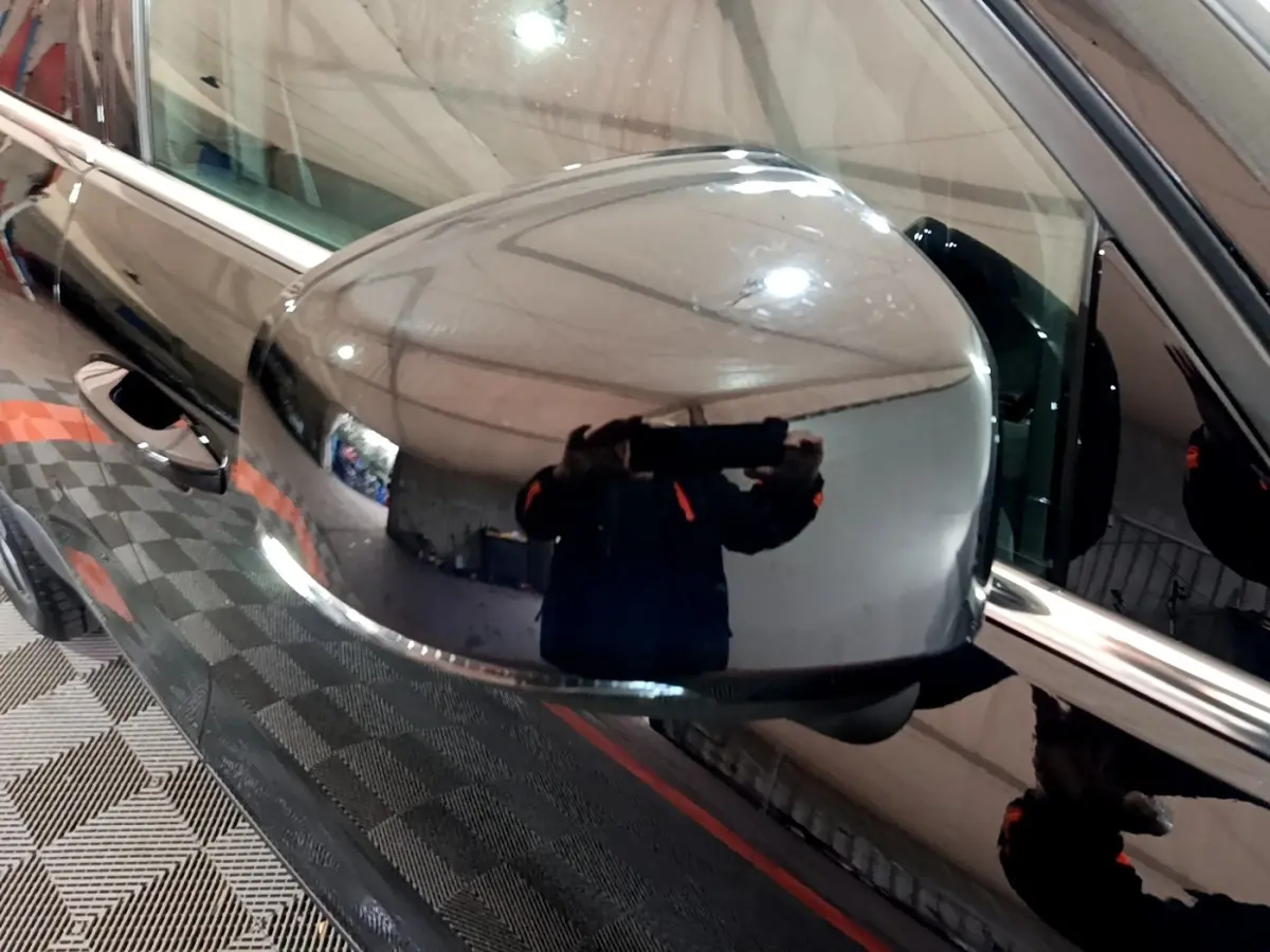 Rétroviseur côté gauche noir brillant du Volvo XC40 Recharge T4 Business, reflet d'un intérieur d'atelier visible.