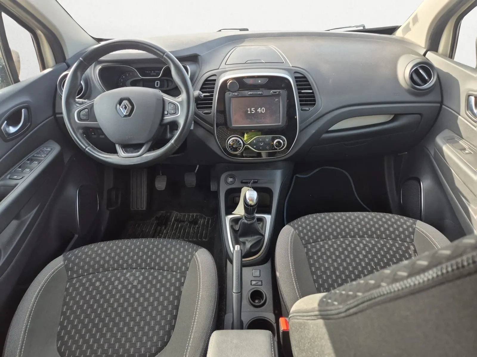 Vue intérieure avant du Renault Captur 2018 montrant le tableau de bord noir, volant multifonction et levier de vitesse manuel.