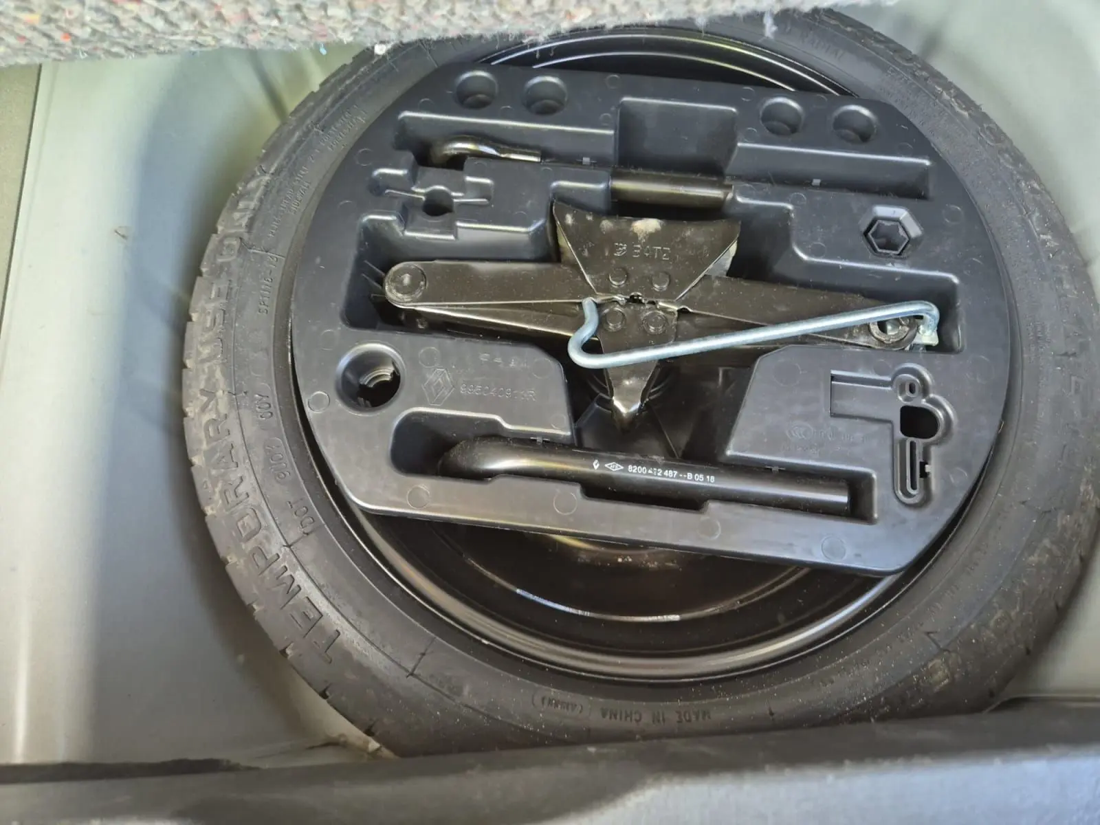 Gros plan sur la roue de secours et le cric noir dans le coffre du Renault Captur beige/marron 2018.