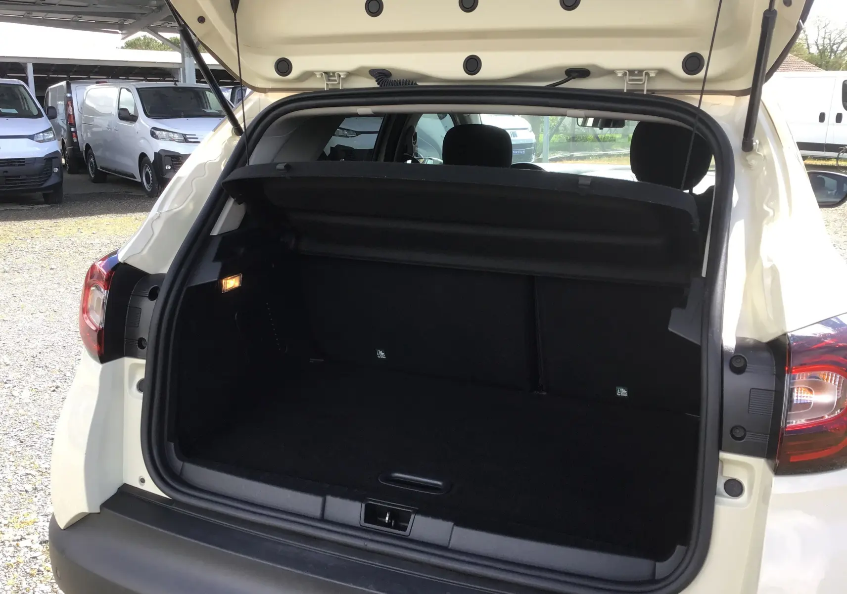Coffre ouvert vu de l'arrière d'un Renault Captur beige/marron, montrant l'espace de chargement vide et la plage arrière.