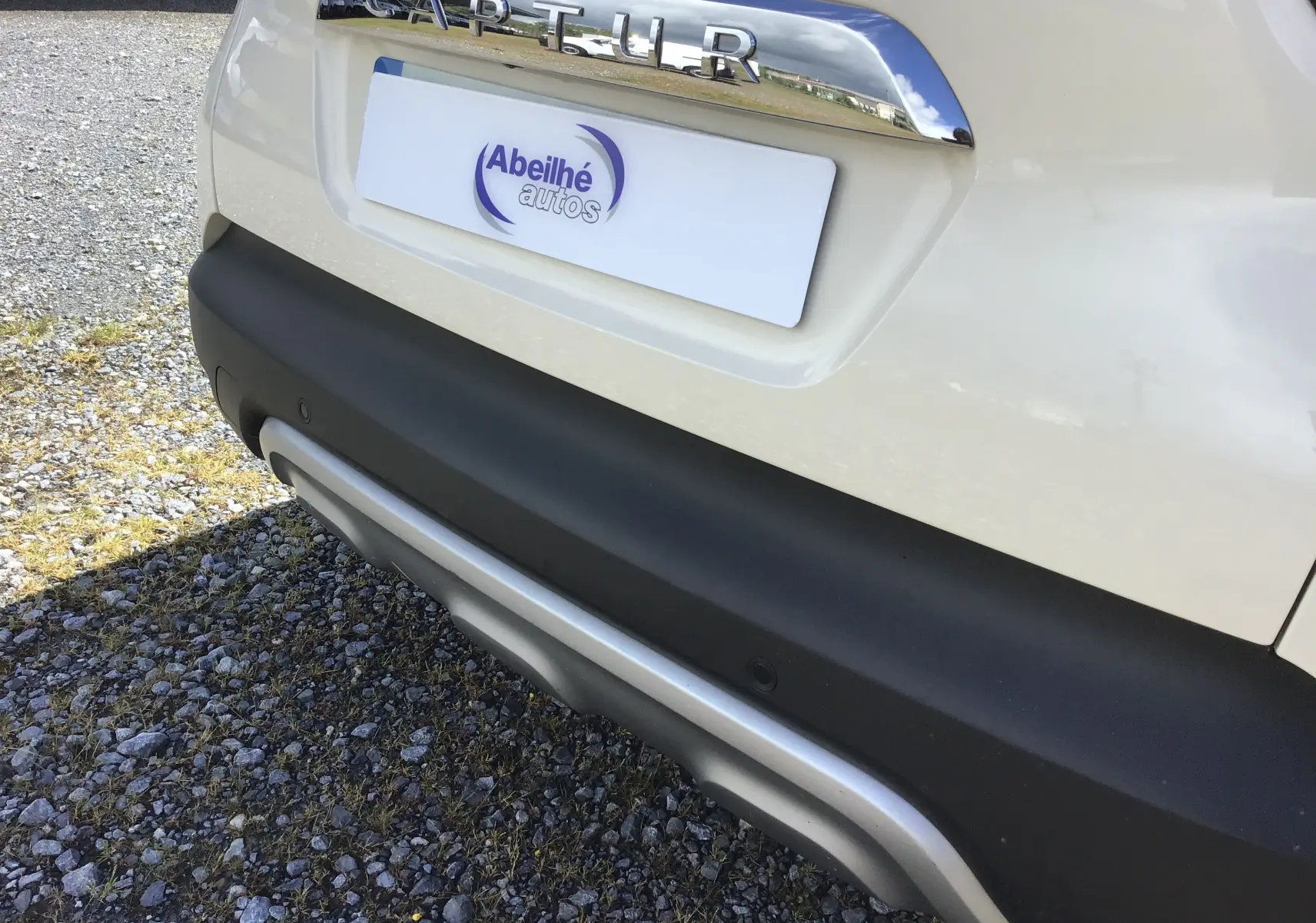 Gros plan sur la partie arrière beige du Renault Captur 2018, mettant en valeur le logo chromé et le pare-chocs noir avec insert argenté.