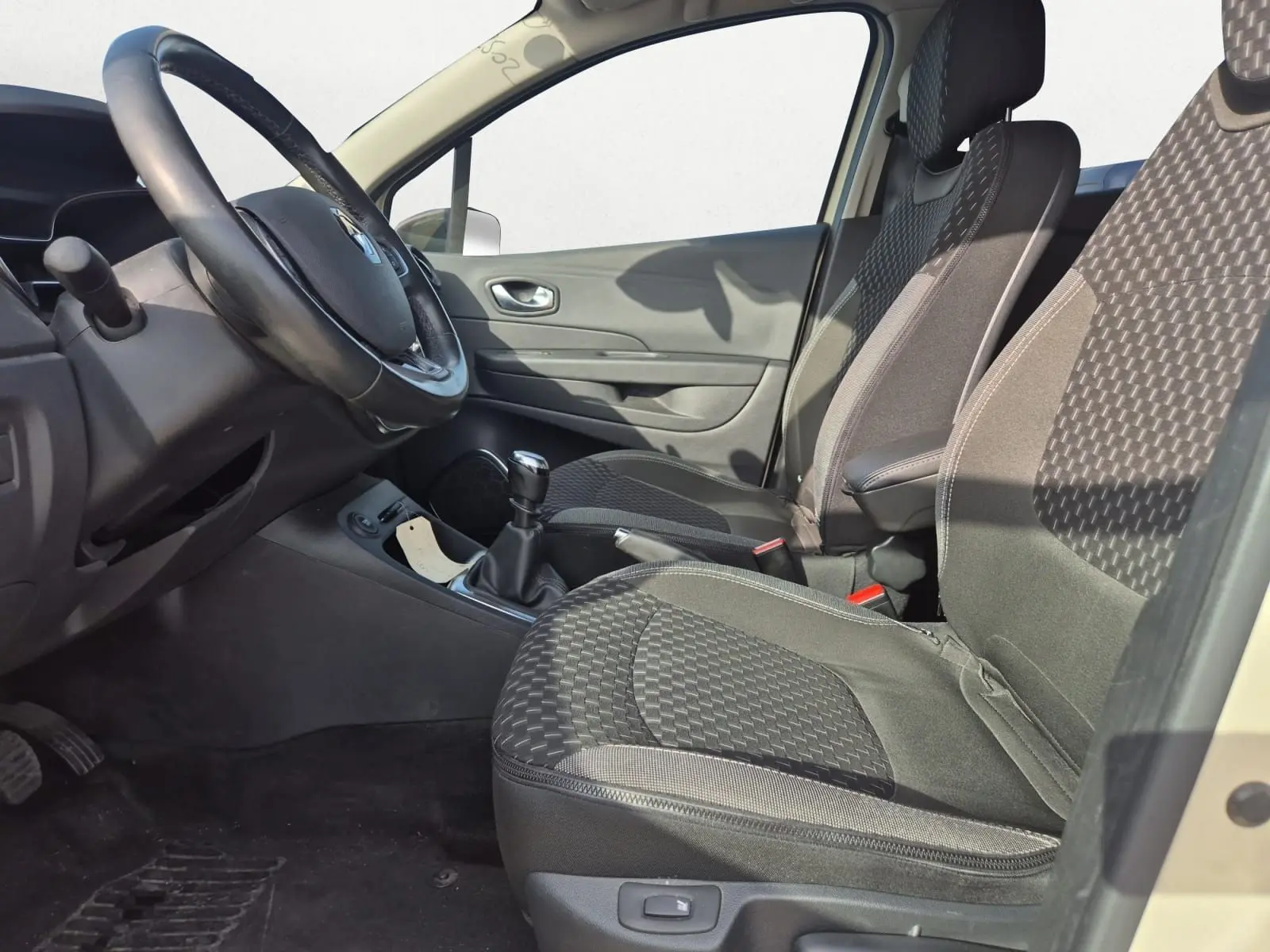 Vue intérieure côté gauche du Renault Captur 2018, sièges tissu noir à motifs, volant cuir et levier de vitesse manuel.
