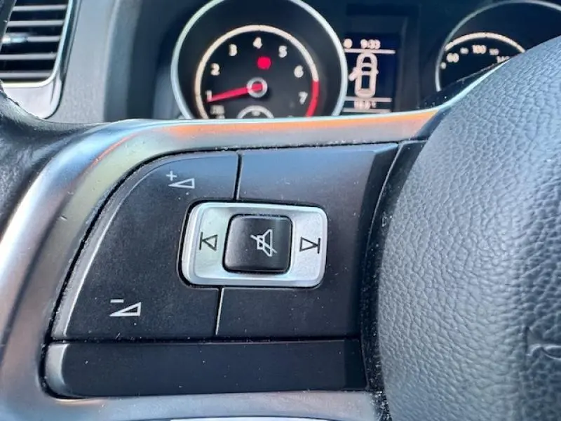 Gros plan sur les commandes audio au volant cuir noir de la Volkswagen Scirocco 1.4 TSI 2017, avec tableau de bord en arrière-plan.