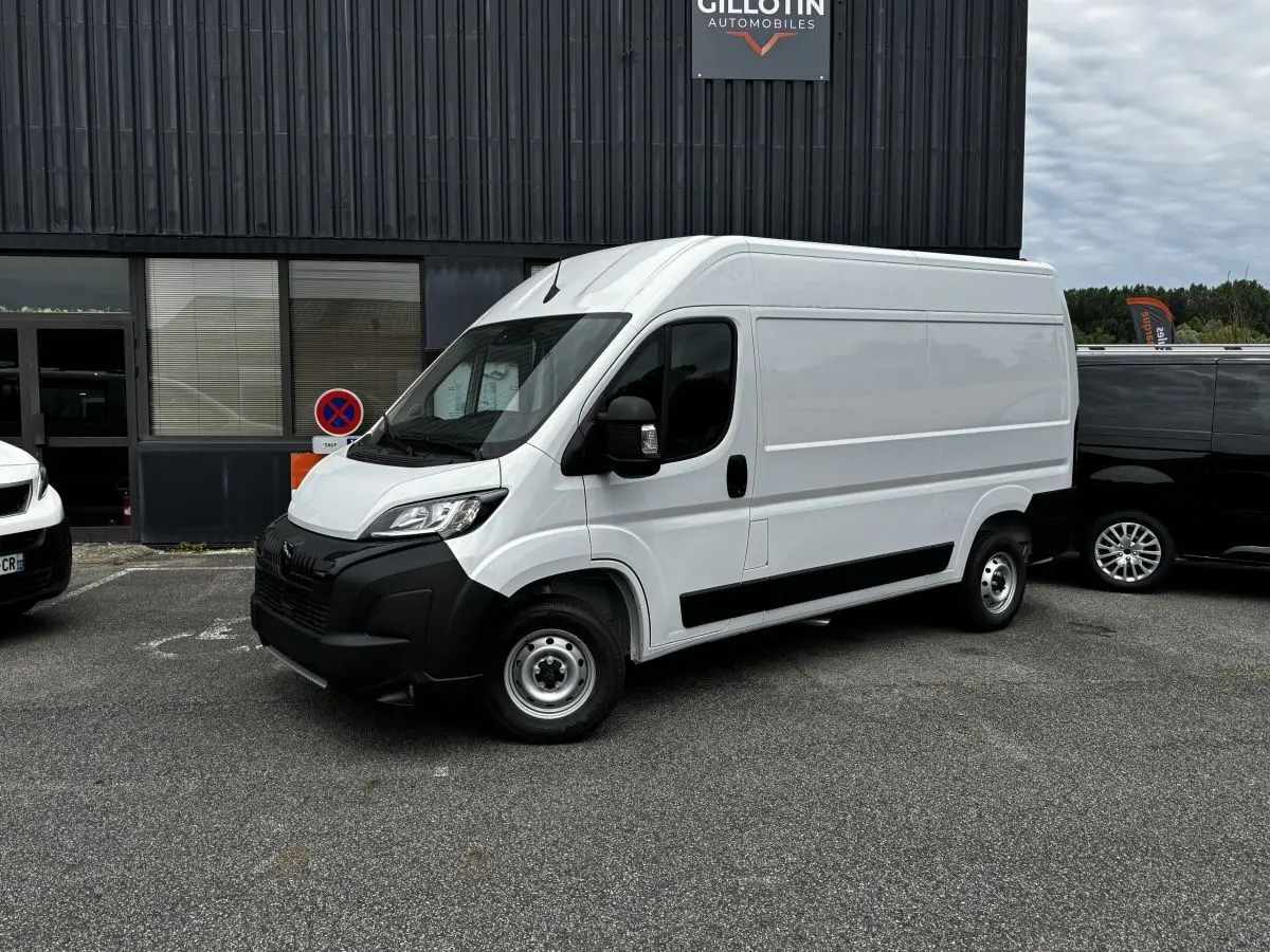 Vue 3/4 avant droite d’un Peugeot Boxer Fourgon blanc avec pare-chocs noir et jantes acier, stationné devant un bâtiment.