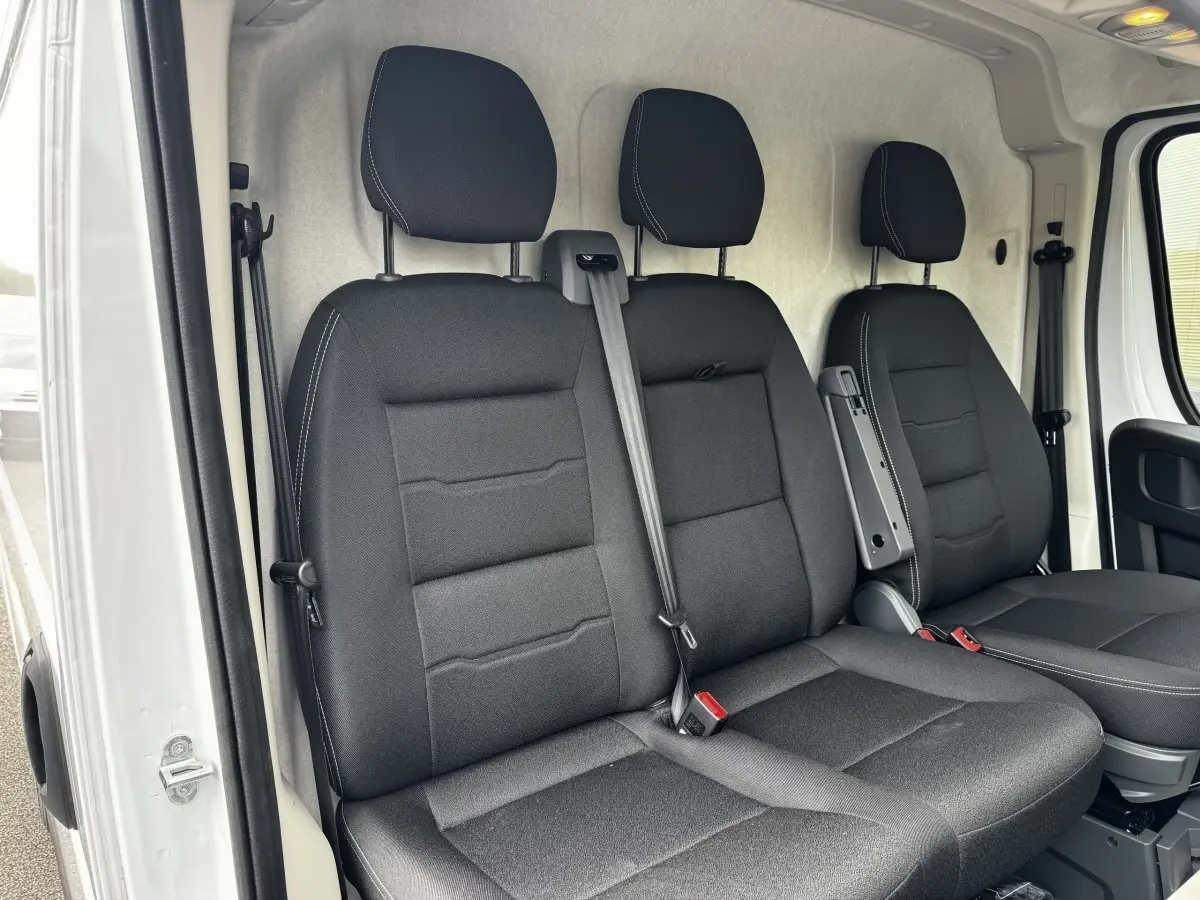 Vue intérieure côté conducteur du Peugeot Boxer Fourgon blanc 2026, montrant les sièges avant noirs avec accoudoir central.
