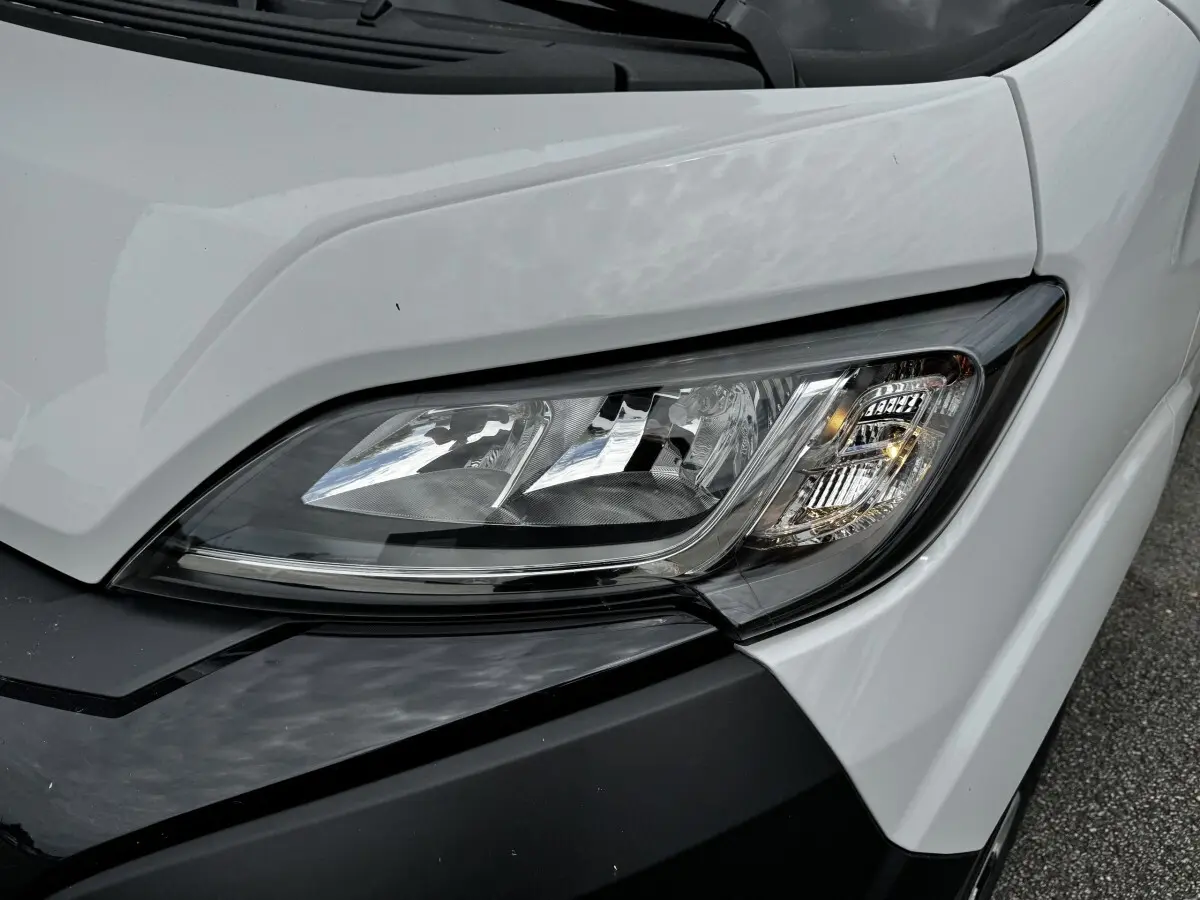 Gros plan sur le phare avant droit du Peugeot Boxer Fourgon blanc, soulignant les détails du bloc optique moderne.