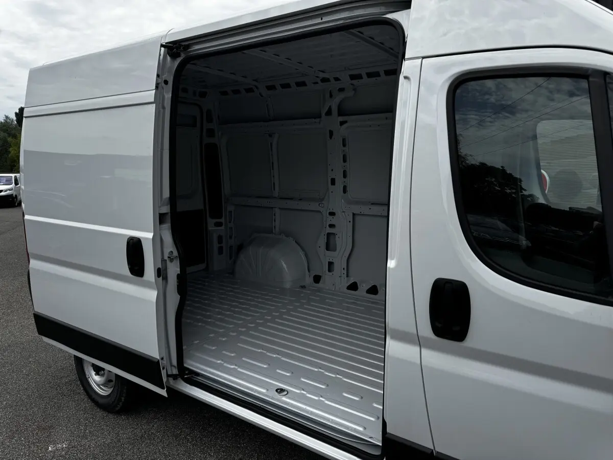 Vue 3/4 avant droit du Peugeot Boxer Fourgon blanc avec porte latérale coulissante ouverte montrant l’espace de chargement vide.