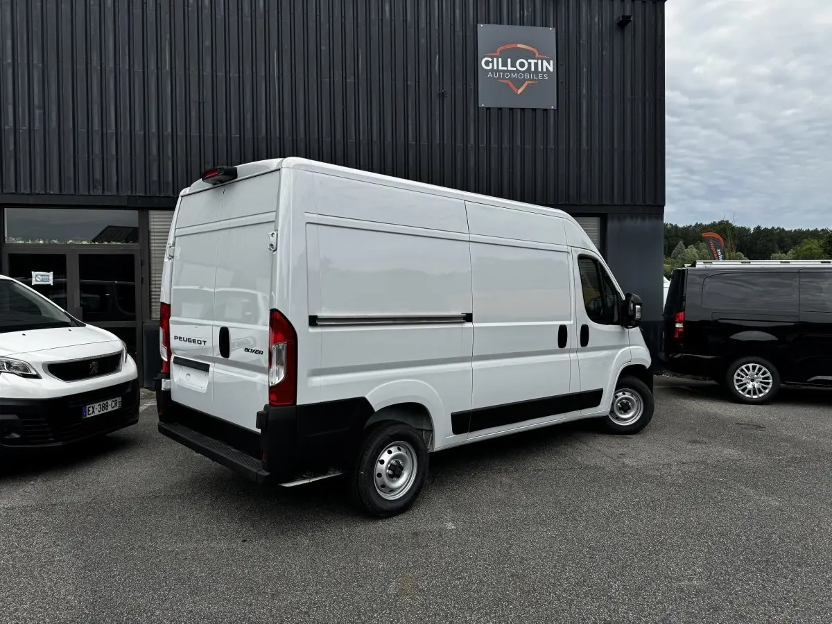 Vue 3/4 arrière droite d’un Peugeot Boxer Fourgon blanc stationné devant un bâtiment avec logo Gillotin Automobiles.
