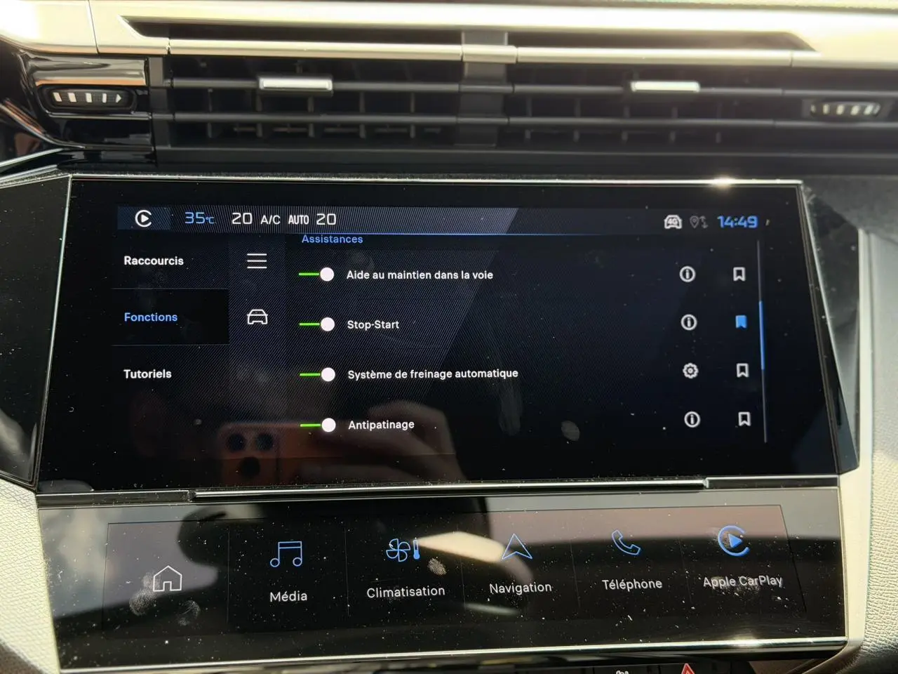 Écran tactile central de la Peugeot 308 Hybrid 2025 affichant les assistances à la conduite, avec commandes climatisation et multimédia.
