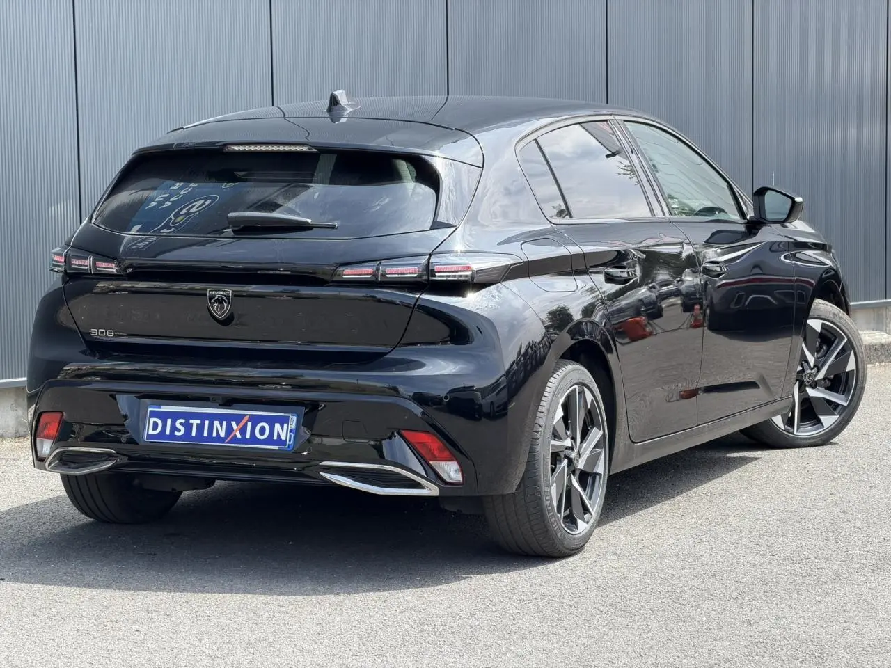 Vue 3/4 arrière droite d'une Peugeot 308 Hybrid 145 noire Perla avec jantes alliage 17 pouces et feux LED distinctifs.