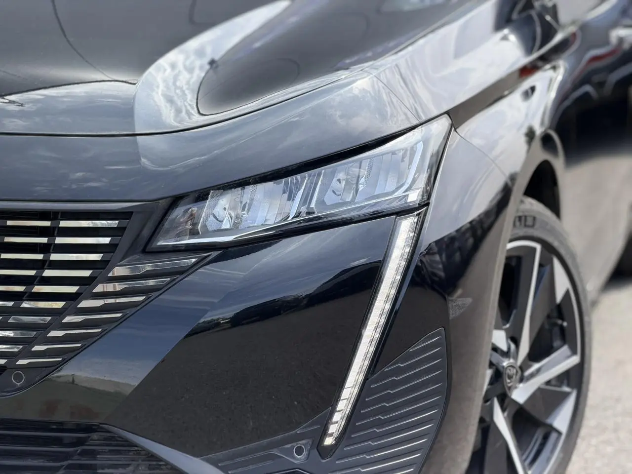 Gros plan sur l'avant droit noir Perla de la Peugeot 308 Hybrid 145 avec feux LED et jante alliage 17 pouces.