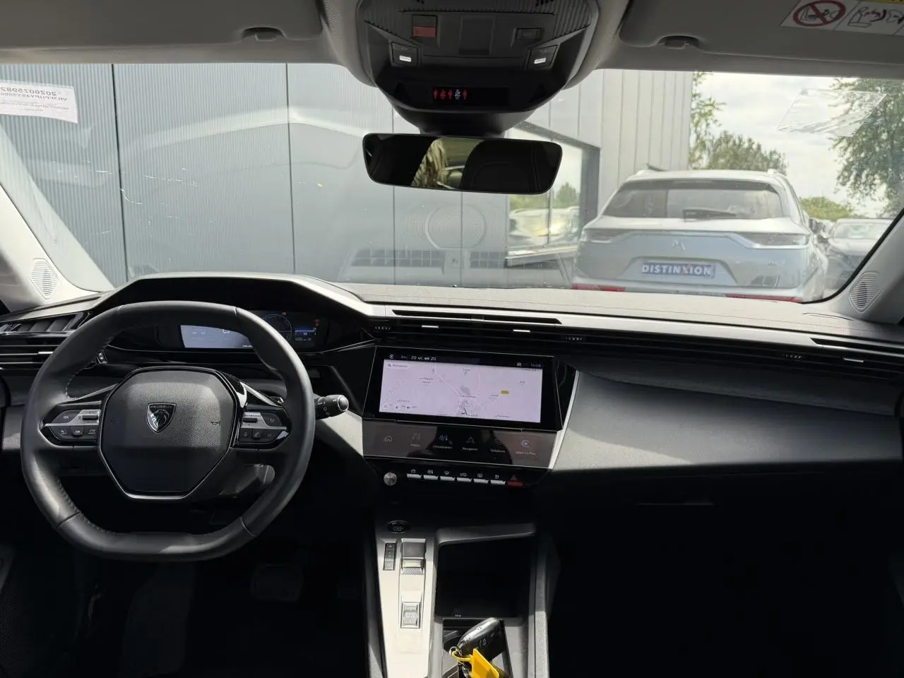 Vue intérieure avant du Peugeot 308 Hybrid 2025, tableau de bord noir avec écran tactile central et volant compact.