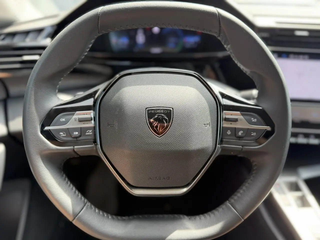 Vue rapprochée du volant cuir noir de la Peugeot 308 Hybrid 2025 avec commandes intégrées et logo central lion.