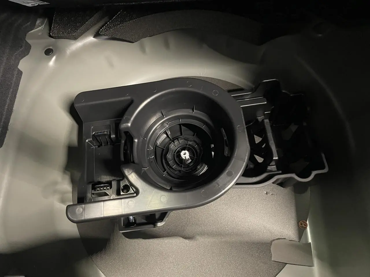 Gros plan sur le compartiment de rangement du kit de dépannage pneumatique dans le coffre d’une Peugeot 208 noire métallisée.