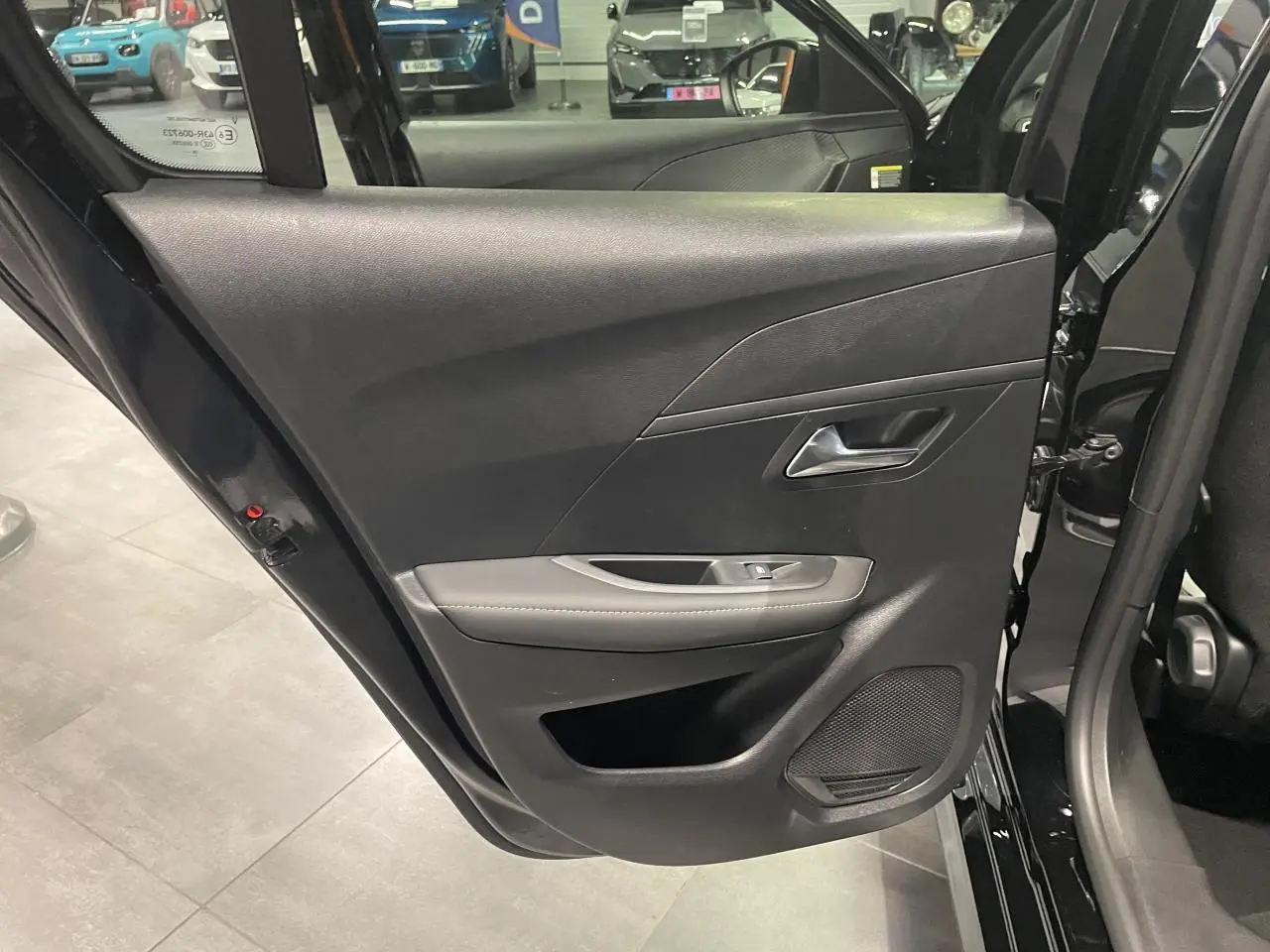 Porte arrière gauche ouverte de Peugeot 208 noire métallisée, montrant la garniture intérieure avec commande de vitre et haut-parleur.