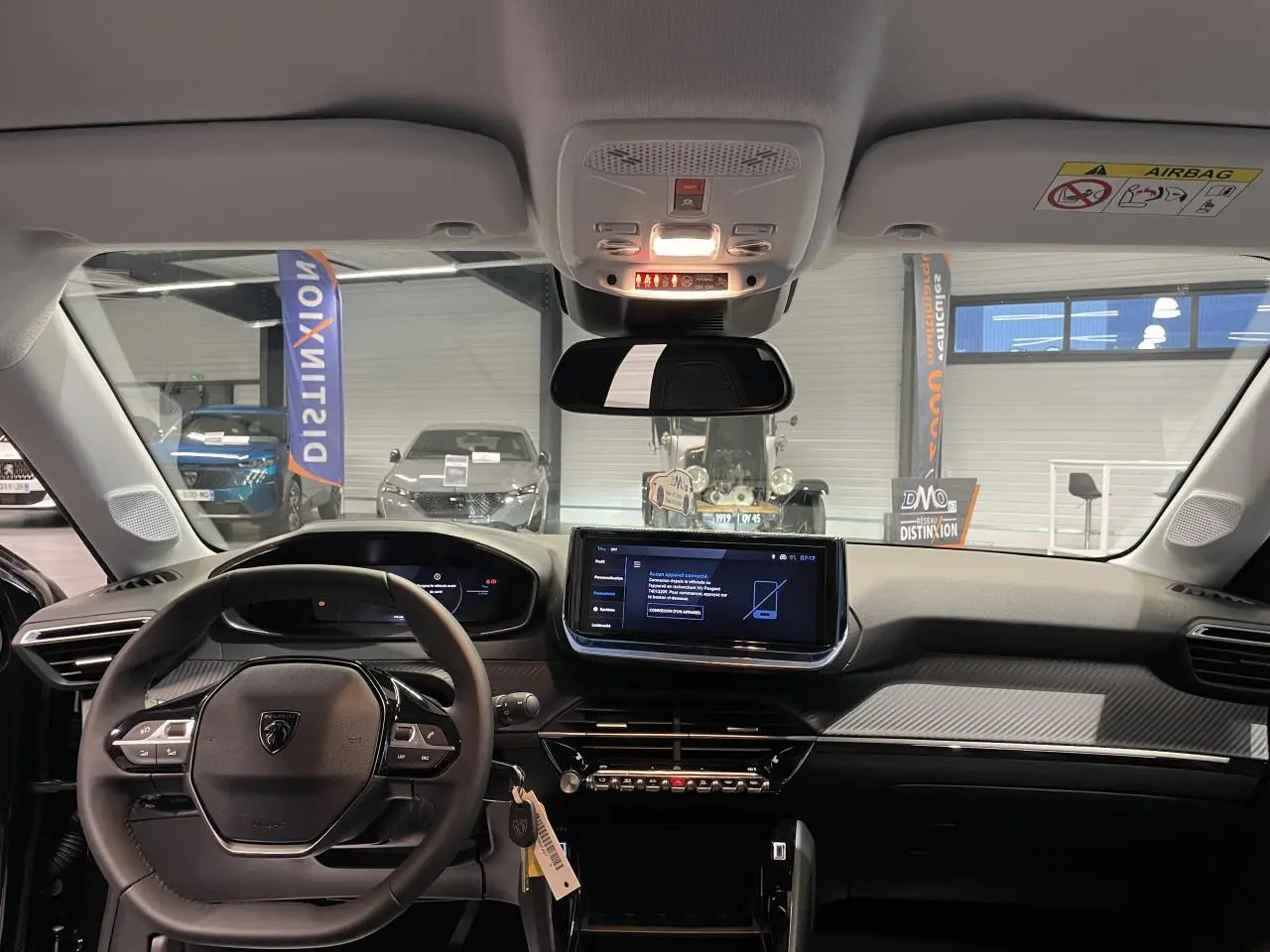 Vue intérieure frontale du Peugeot 208 1.2i Hybrid 2025, tableau de bord noir avec écran tactile central et volant compact.