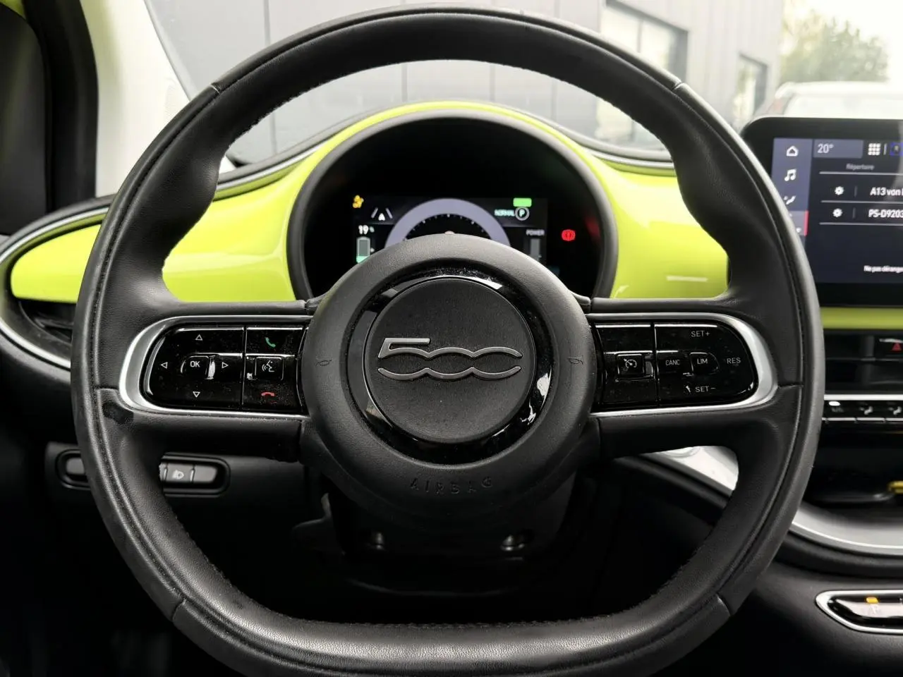 Vue centrée sur le volant noir de la Fiat 500 électrique 2024, avec tableau de bord et garniture jaune Acid en arrière-plan.