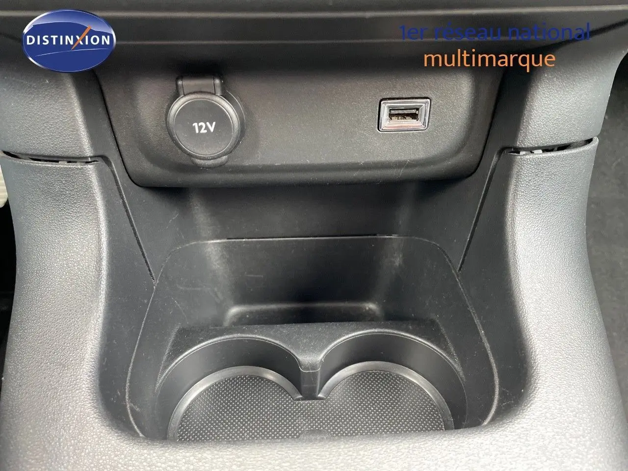 Gros plan sur la console centrale noire du Citroën C3 2021 montrant prise 12V et port USB au-dessus des porte-gobelets.