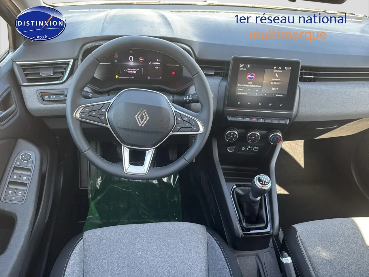 Vue intérieure centrée sur le volant cuir et la console centrale avec levier de vitesse manuelle de la Renault Clio V gris rafale.