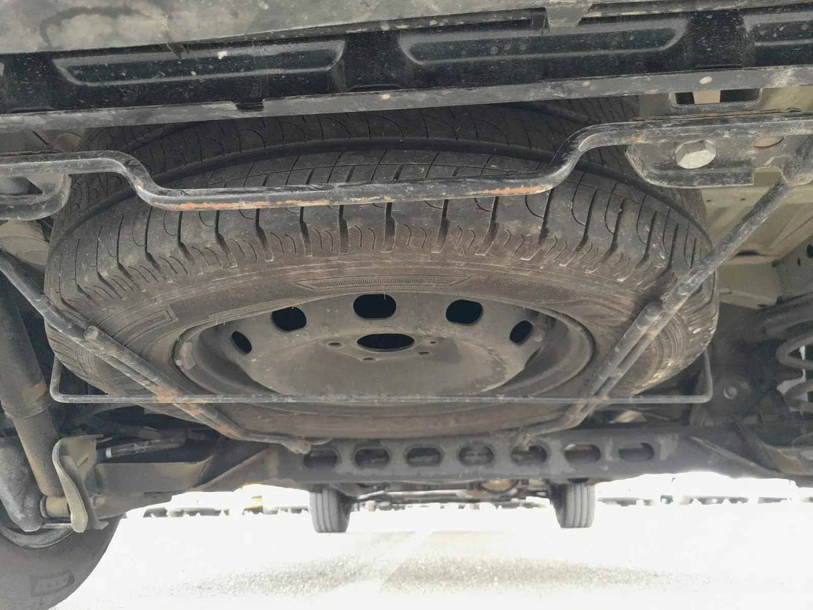 Vue en contre-plongée sous un Renault Trafic Combi gris foncé, montrant la roue de secours fixée sous le châssis.