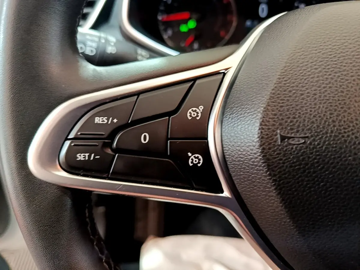 Gros plan sur les commandes du régulateur de vitesse au volant cuir noir de la Renault Clio Business blanche de 2019.